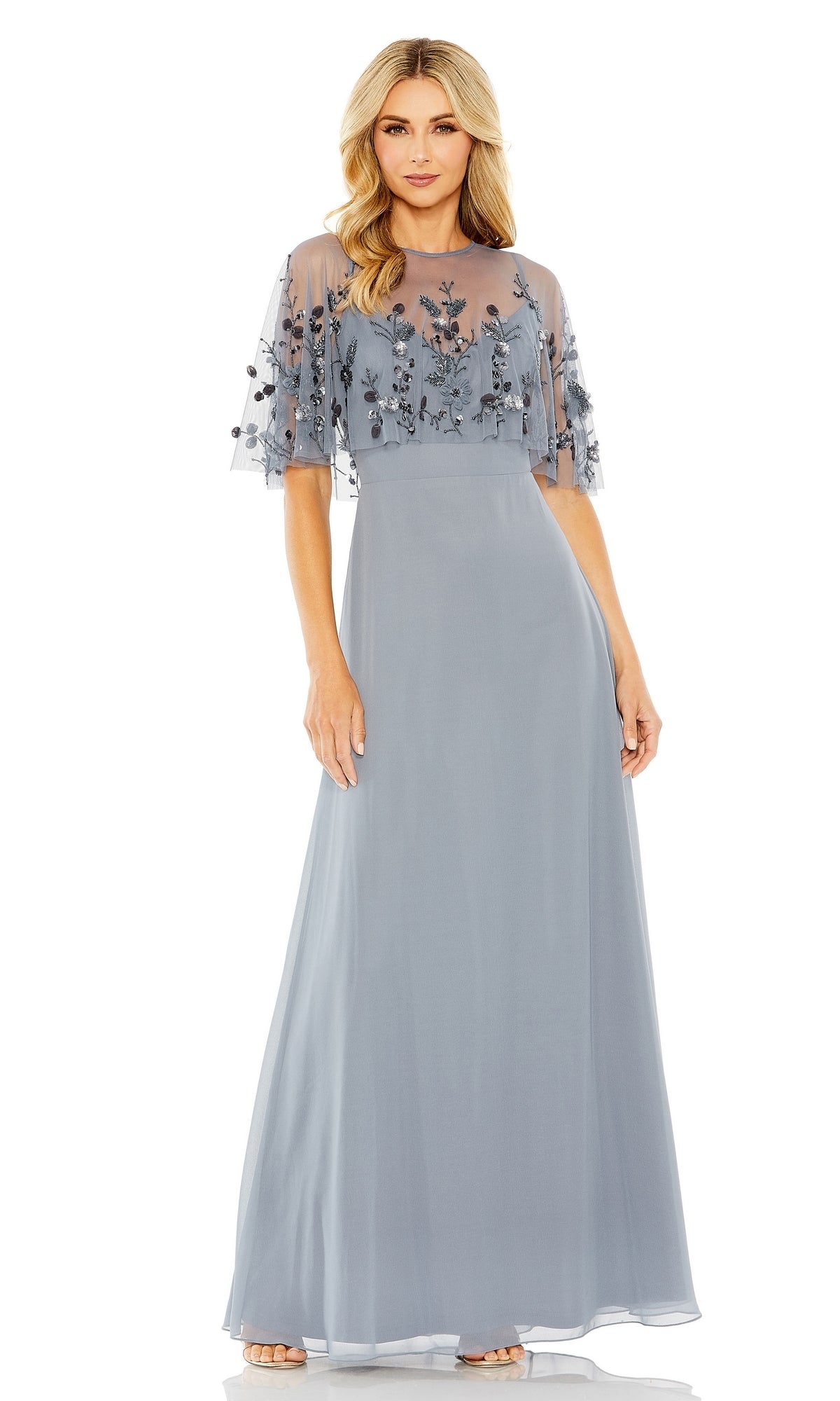 Woman in a floor-length, light blue Mac Duggal 9229 prom dress with sheer embroidered short sleeves and bodice, standing against a white background.